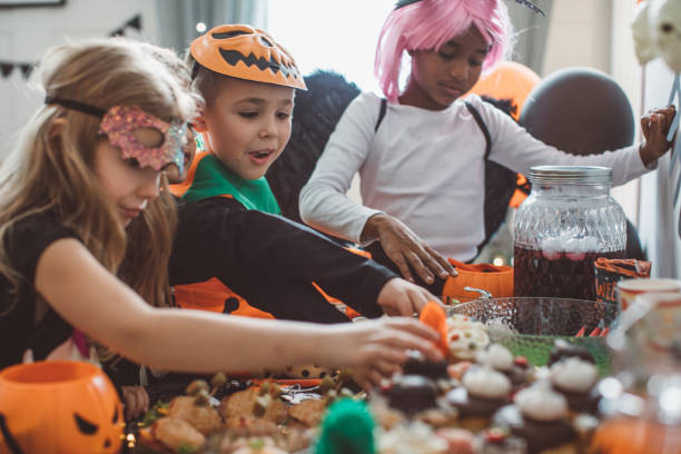 Multi ethnic group of children have party at home, they wear costumes, celebrating Halloween and enjoy in spooky food